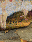 Close-up of a textured fabric bag with a Degas signature on a stone background