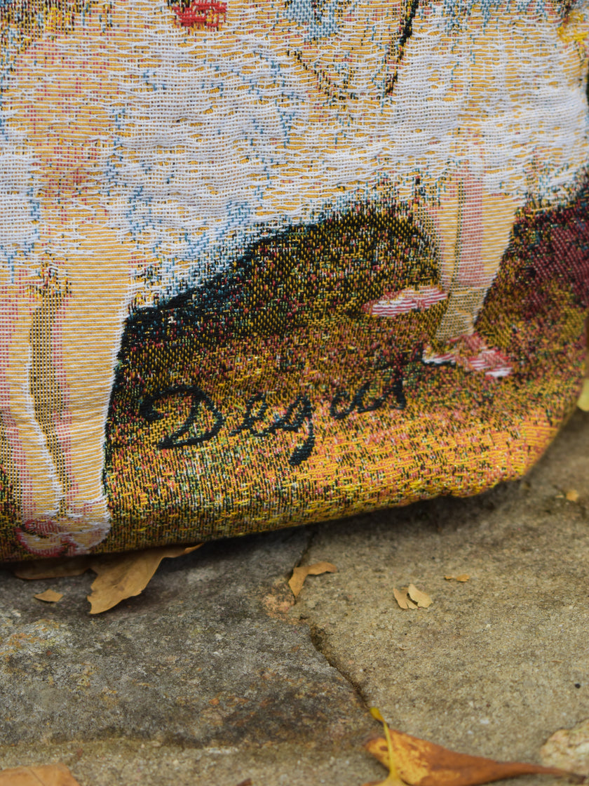 Close-up of a textured fabric bag with a Degas signature on a stone background