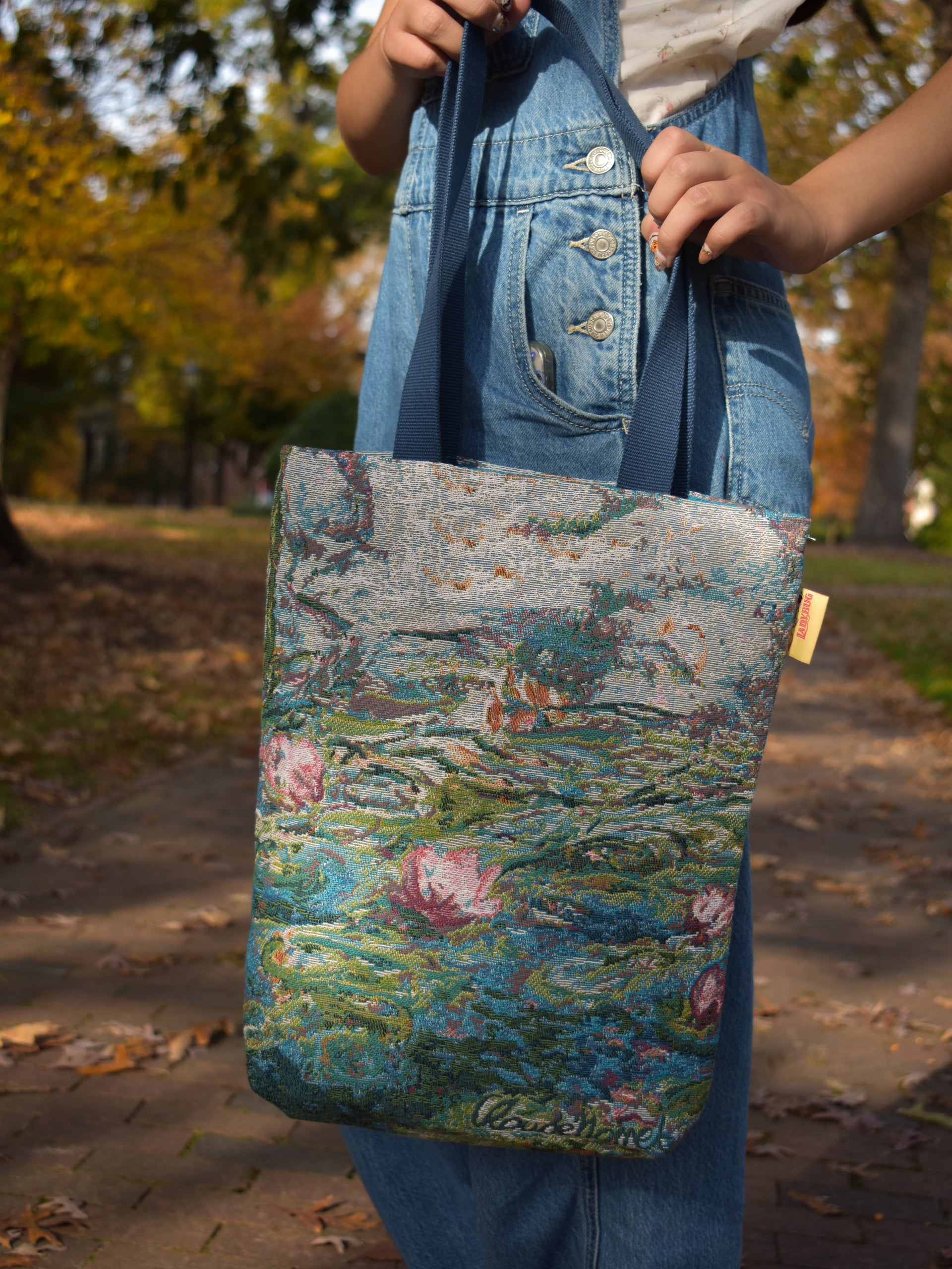 Person holding a tote bag with a floral design in an outdoor setting claude monet water lilies nympheas tote bag artwork masterpiece