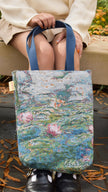 Person holding a Claude Monet water lilies tote bag with a floral design, sitting on a bench outdoors.