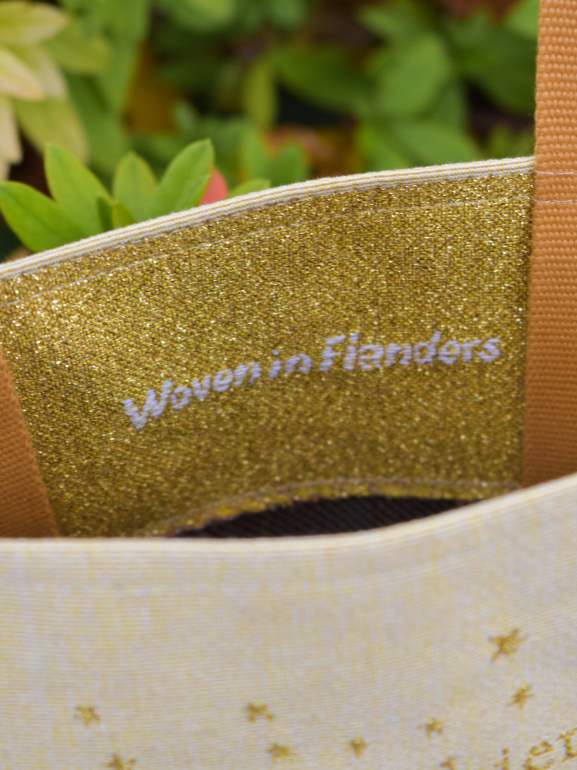 Gold glittery label with 'Woven in Flanders' text on a fabric background