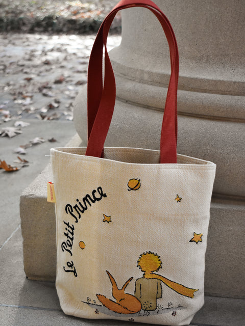 Tote bag with 'Le Petit Prince' design on a stone surface with leaves.