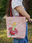 Person holding a pink tote bag with a fairy design outdoors