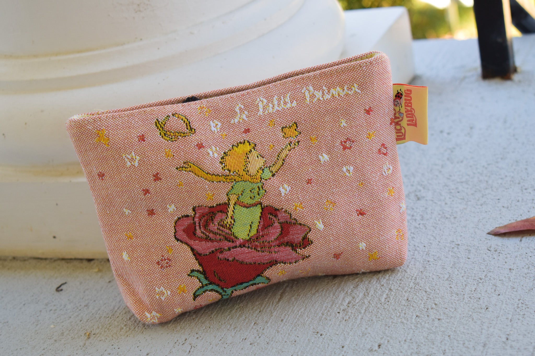 Small pink makeup, toiletries pouch with 'Le Petit Prince' design on a light surface