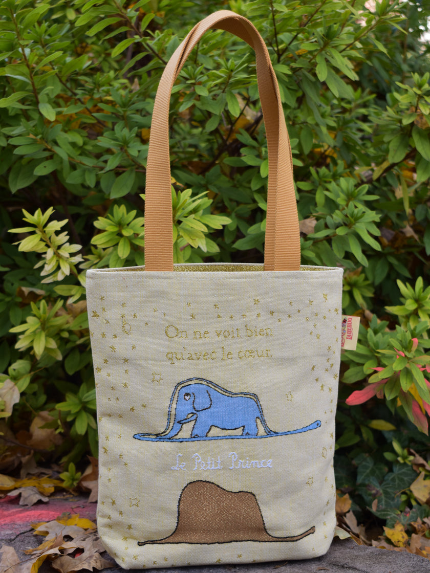 Tote bag with elephant design and text in front of green foliage