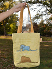 Yellow tote bag with an elephant design held by a hand in a park setting