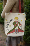 Tote bag with 'Le Petit Prince' design held by a person outdoors.