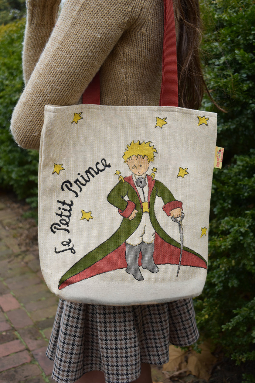 Tote bag with 'Le Petit Prince' design held by a person outdoors.