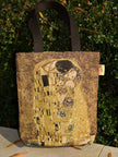 Tote bag with 'The Kiss' artwork by Gustav Klimt against a green bush background