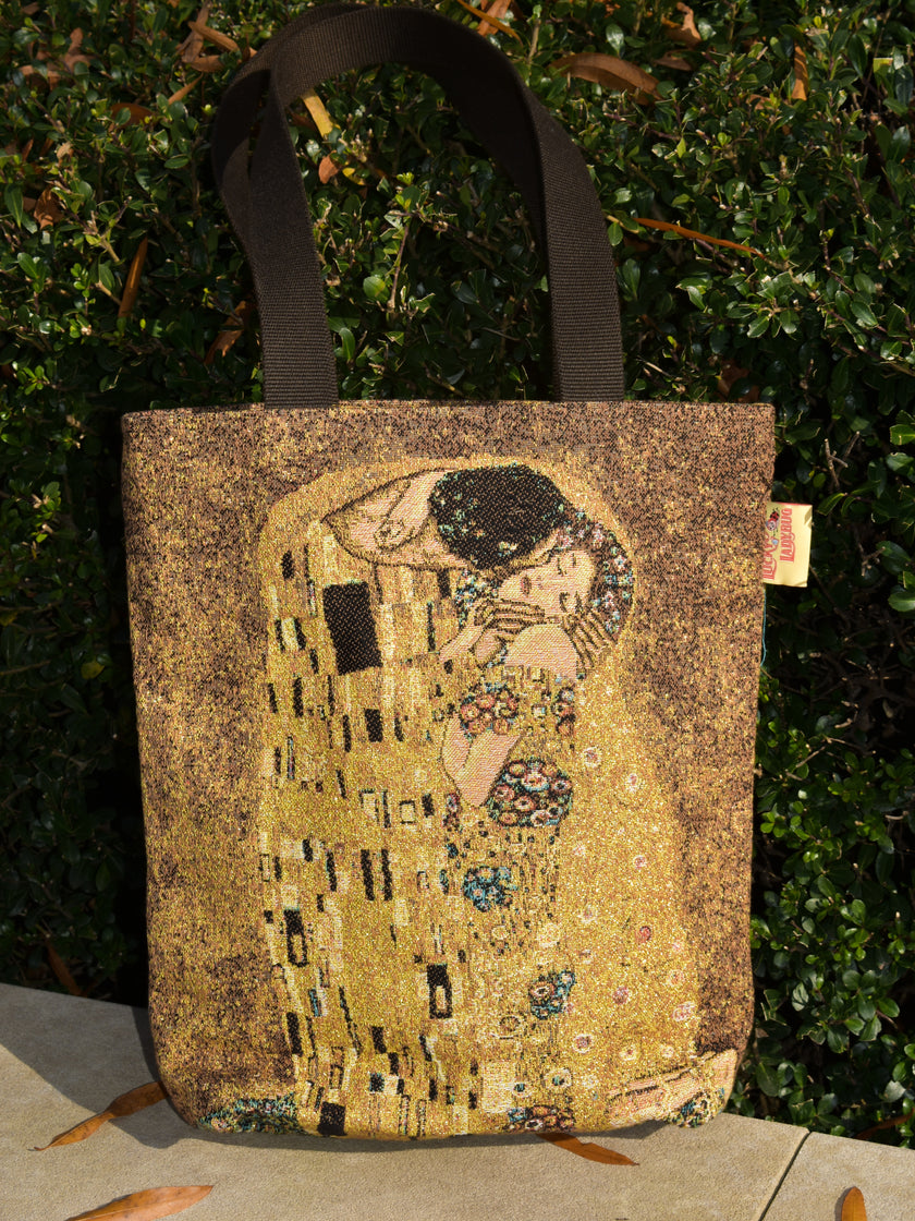 Tote bag with 'The Kiss' artwork by Gustav Klimt against a green bush background