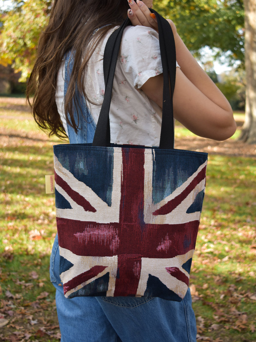 Person holding a tote bag with a Union Jack design outdoors.
